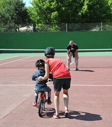 Kind lernt Radfahren auf einem Tennisplatz auf dem Campingplatz in der Vendée