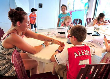 Instructor and child around a table at the children's club of the campsite in Saint-Hilaire-de-Riez